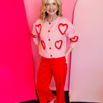 Soft pink button-up cardigan with oversized fuzzy red heart pattern and cozy textured knit.