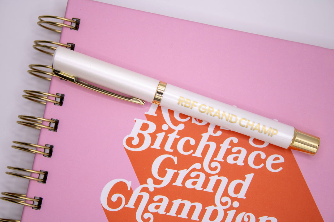 Pen that has “Resting Bitchface Grand Champion,” in gold lettering on a white pen.