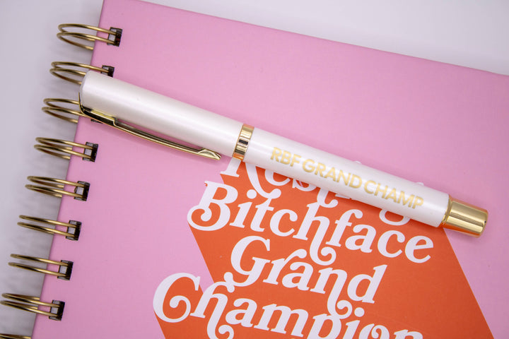 Pen that has “Resting Bitchface Grand Champion,” in gold lettering on a white pen.