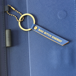 Keychain with 'Bad Bitch Energy' tag attached to a blue folio.
