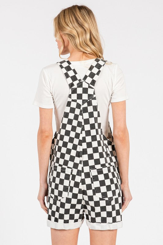 Black checkered knit romper overalls with cuffed shorts, chest and side pockets, and adjustable straps, laid flat to show texture and structure.