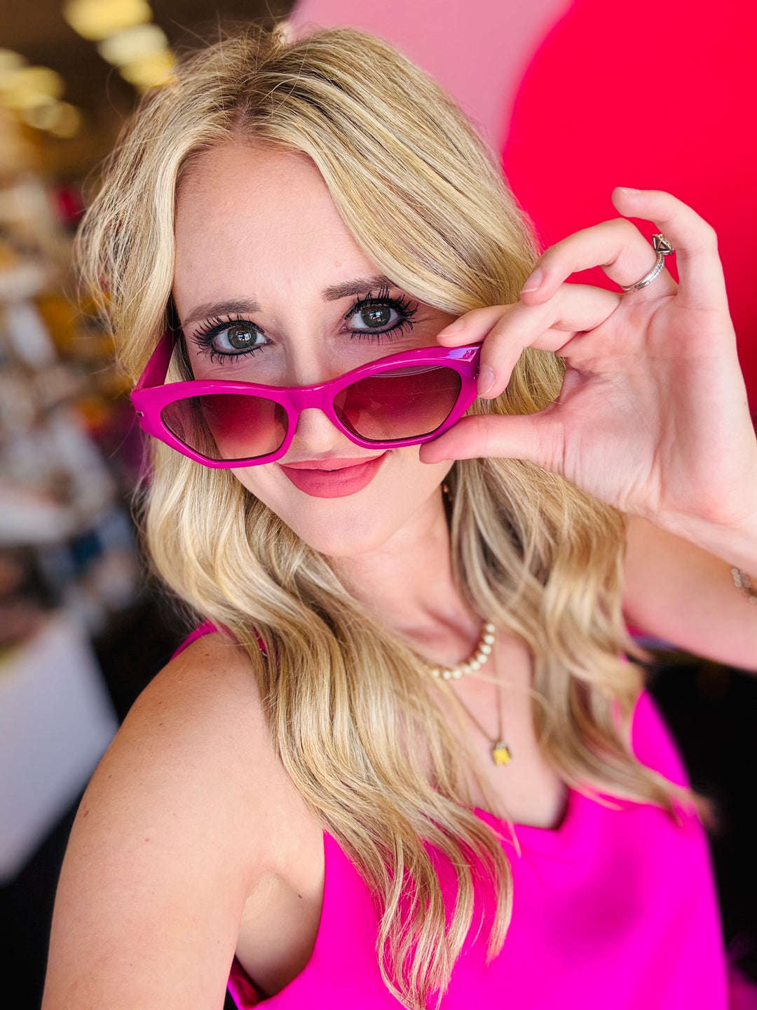 Model playfully posing with Sawtelle Berry Gradient Sunglasses pulled slightly down from eyes, showcasing the bold cat eye shape and vibrant gradient lenses.