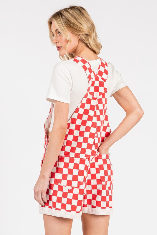 Red checkered knit romper overalls with adjustable straps, metal hardware, multiple pockets, and cuffed shorts, laid flat to highlight color and texture.
