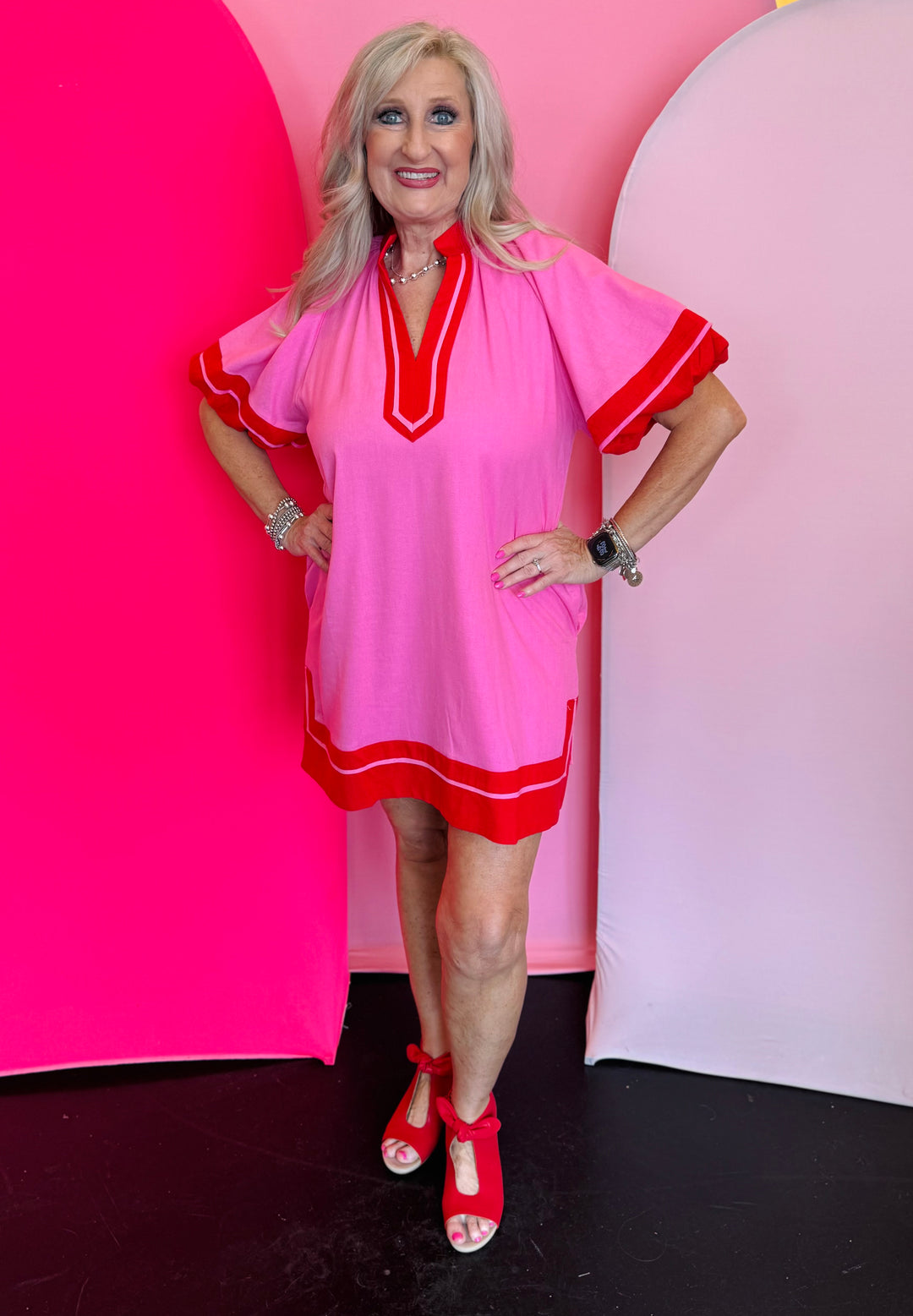 Pink mini dress with short lantern sleeves, a high neck split collar, contrast trim detailing, and a side slit hem, displayed on a model standing confidently.