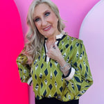 Olive, navy, and cream diamond-print blouse with ruffled neckline, contrast trim, and long elastic-cuff sleeves.