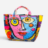 Glossy PVC tote bag with colorful pink, blue, yellow, orange, and purple abstract face design.