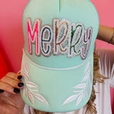 Mint trucker hat with colorful sequin “Merry” patch and white embroidered leaf accents on brim.