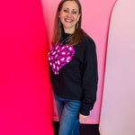Black sweatshirt with bold pink and white leopard heart graphic and classic cozy crewneck fit.