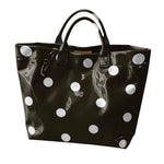 Black tote bag with oversized white polka dots and sturdy top handles.