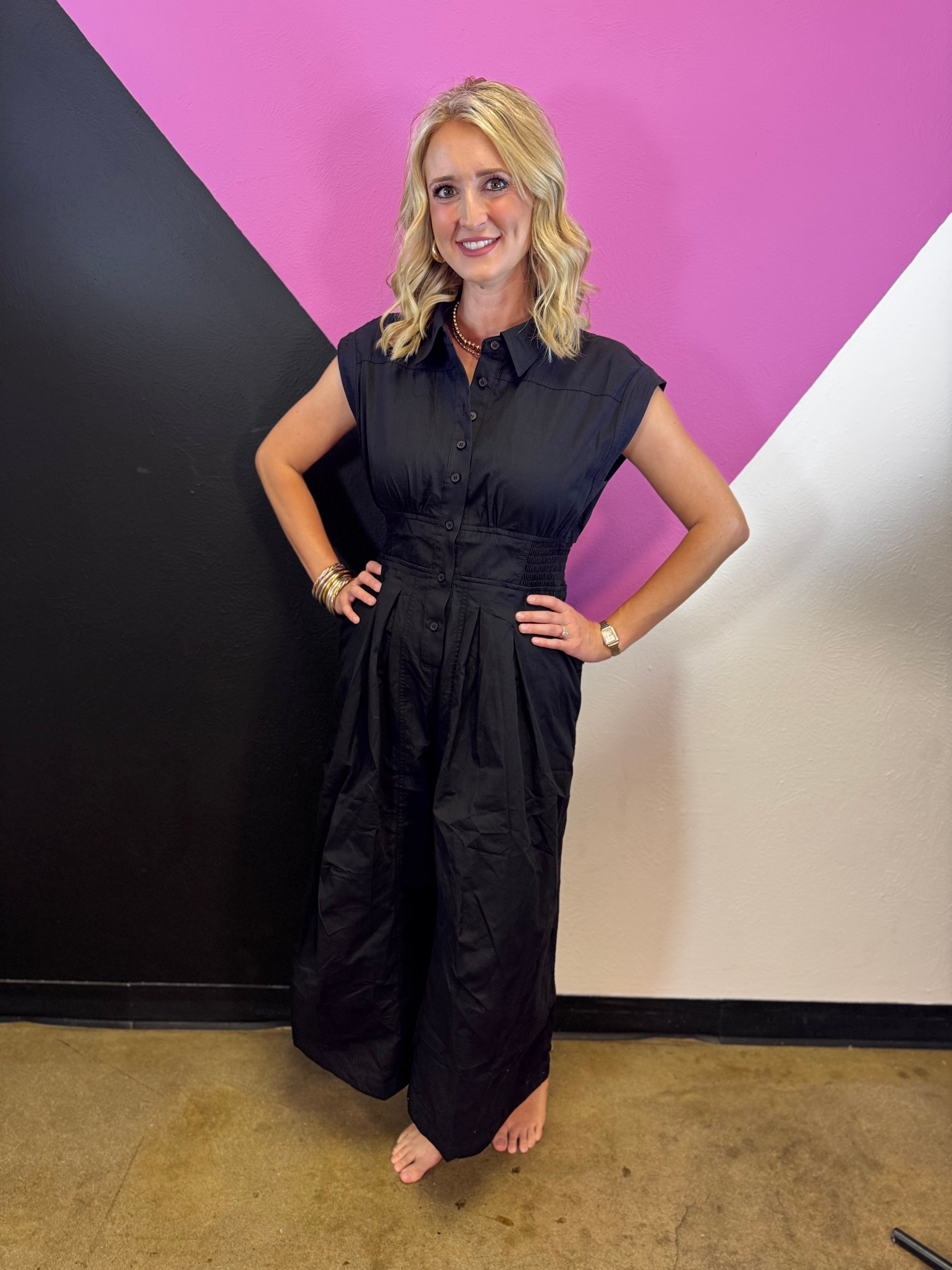 Black wide leg romper with collared neckline, button front, elastic waist, and side pockets.
