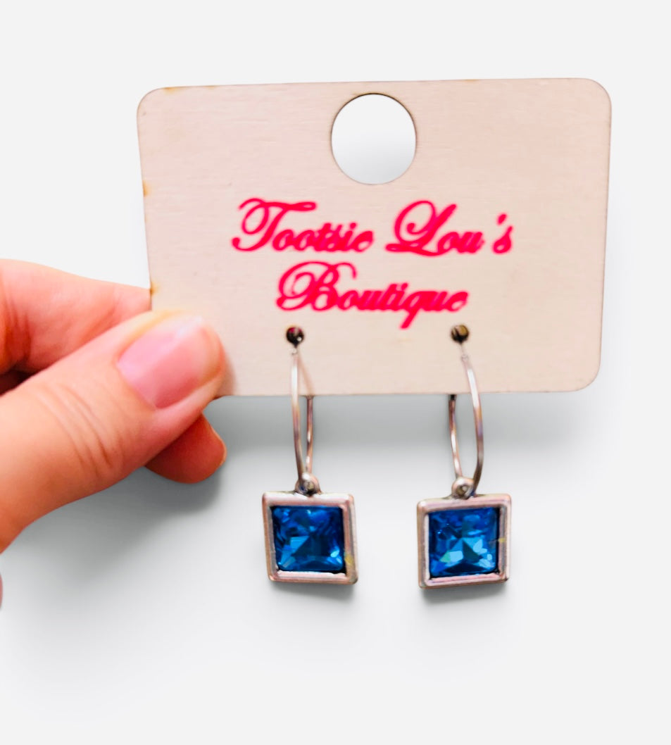 Faceted blue square crystal drop earrings suspended from polished silver-tone hoops.