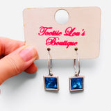Faceted blue square crystal drop earrings suspended from polished silver-tone hoops.