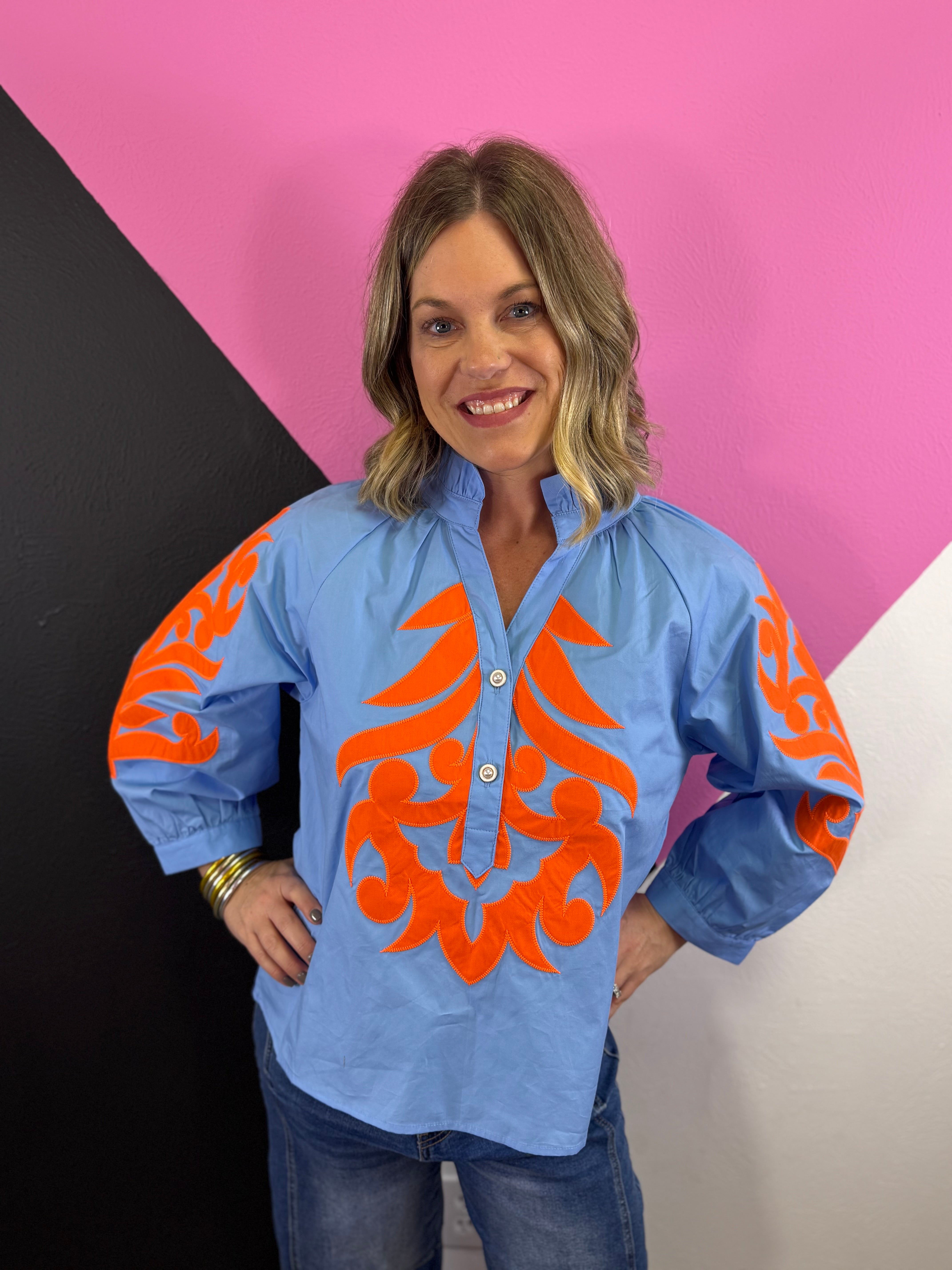 Light blue top with orange scroll print, ruffled neckline, and puff sleeves.