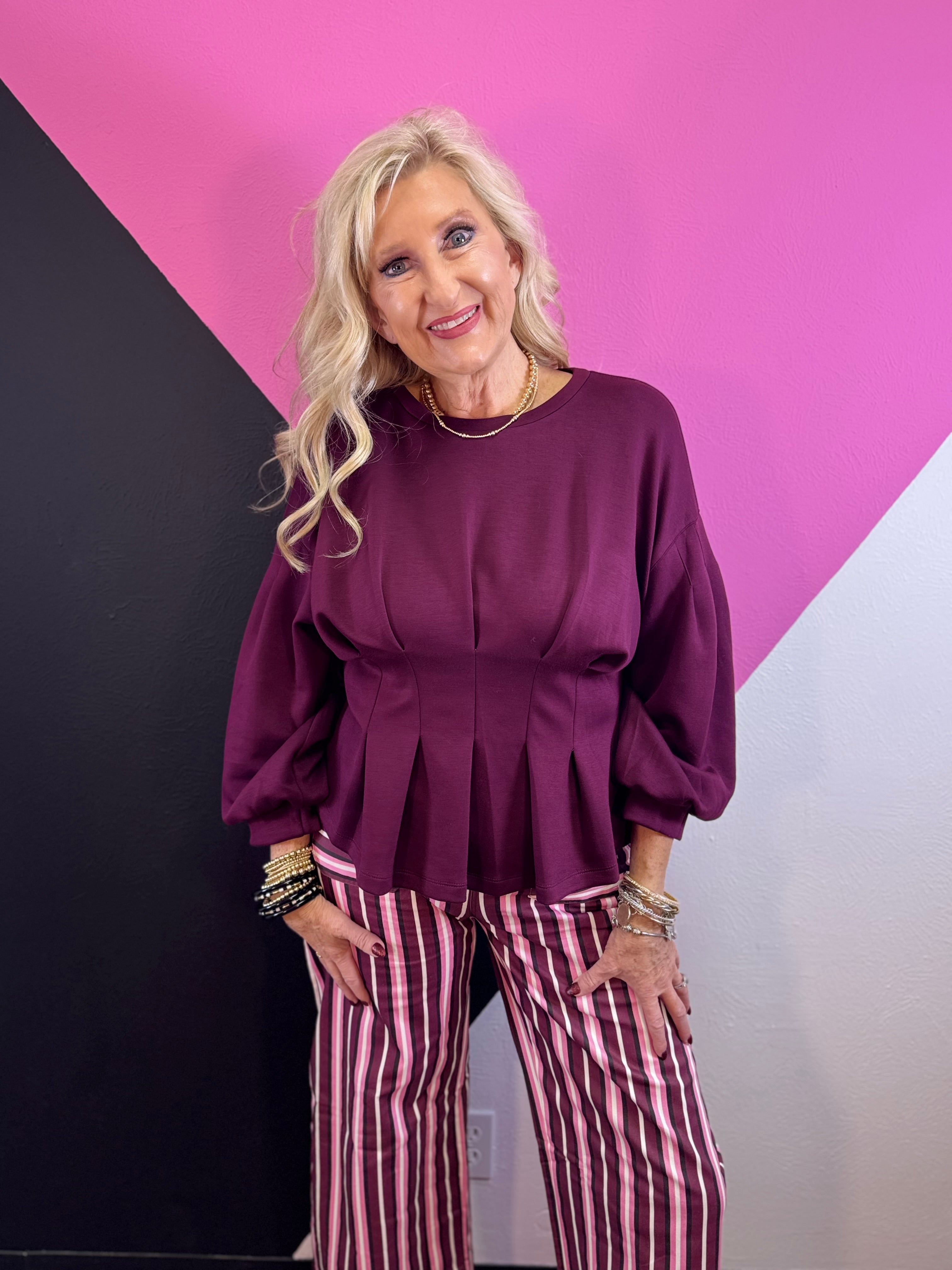 Burgundy peplum top with pleated waist, round neckline, and long balloon sleeves.