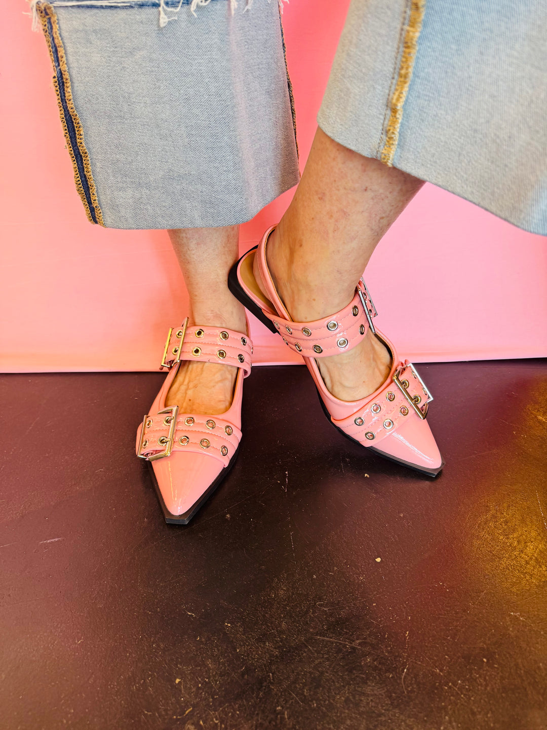 Pink pointed-toe flats with bold silver double buckle straps and a slingback backstrap, combining vibrant color with edgy charm.