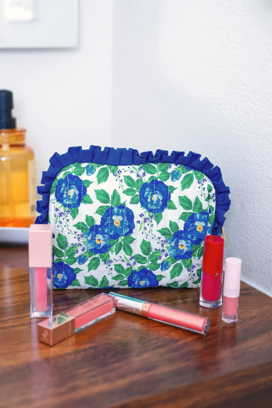 Blue floral quilted bag with ruffle trim and zipper closure.