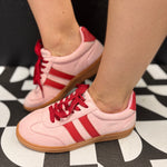 Pink low-top sneakers with bold red stripes, red laces, and retro-inspired styling.