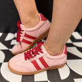 Pink low-top sneakers with bold red stripes, red laces, and retro-inspired styling.