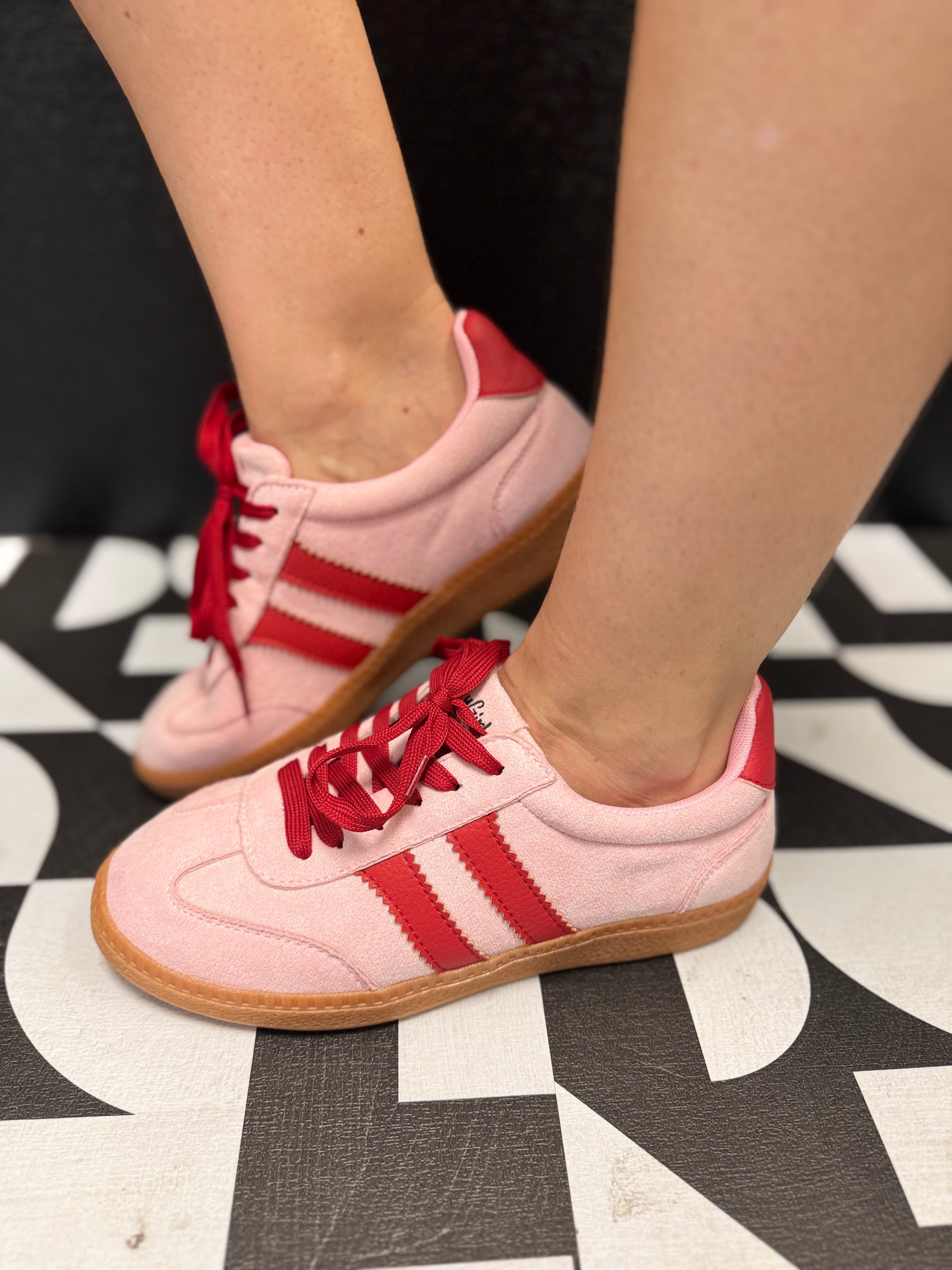 Pink low-top sneakers with bold red stripes, red laces, and retro-inspired styling.