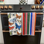 Two Crae hand towels with colorful butterfly and multicolor striped designs.