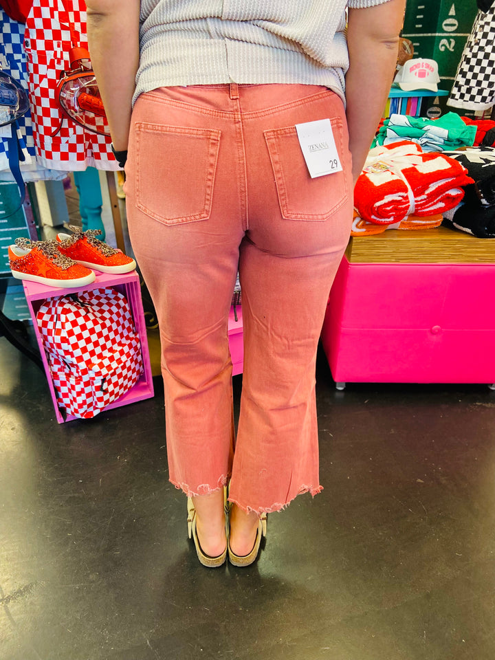Back side of Cabernet colored jeans with cropped length and distressing at knees. Raw hem line.