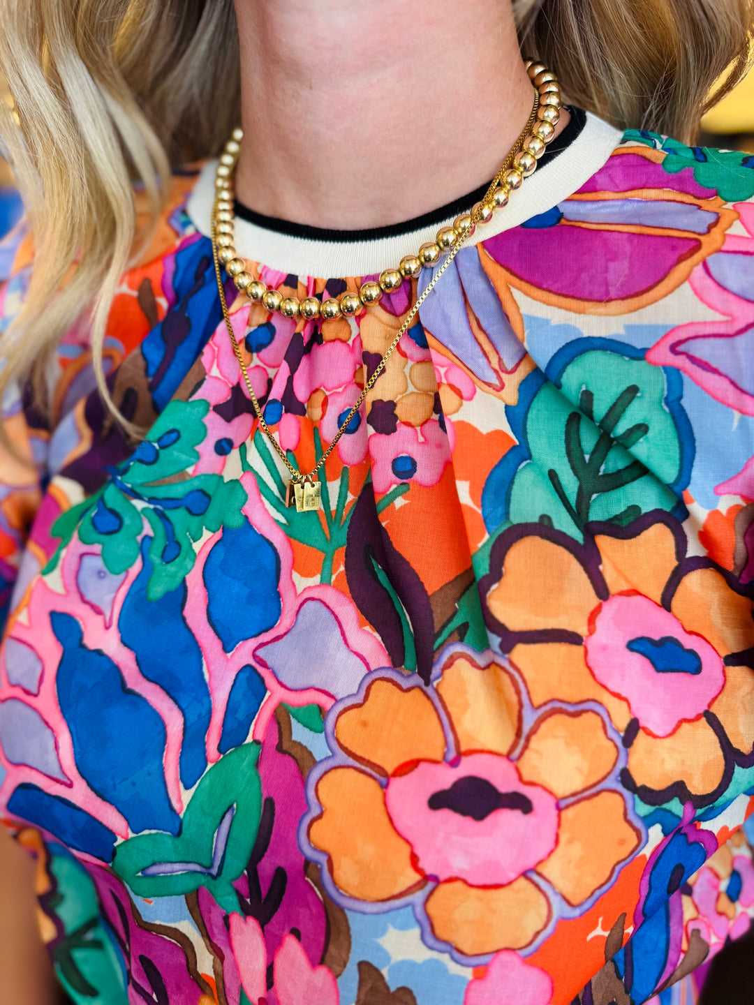 Vibrant floral print top in pink, orange, purple, and green with puff sleeves, round neckline, and contrast trim.