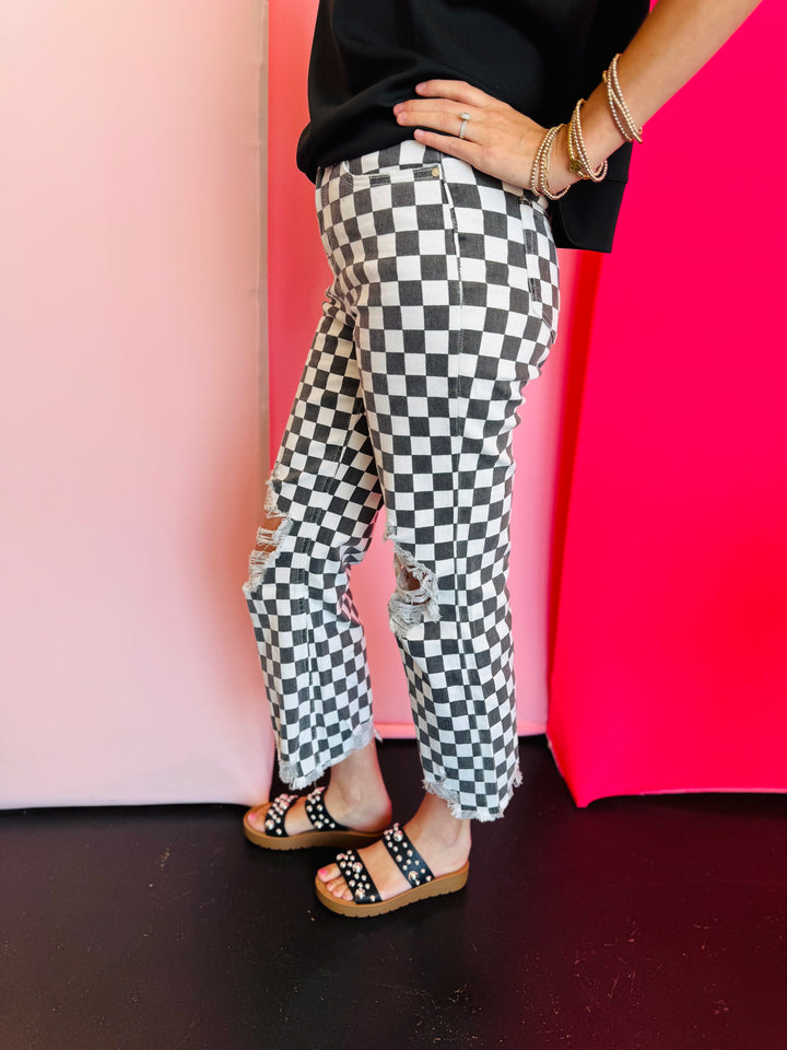 Side view of black and white cropped checkered jeans with knee distressing.
