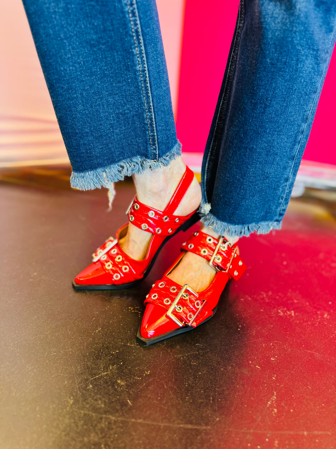 Red pointed-toe flats with bold silver double buckle straps and a slingback backstrap, combining vibrant color with edgy charm.