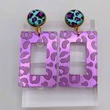 Purple mirror acrylic rectangle earrings with teal and magenta leopard-print stud.