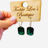 Gold hoop earrings with dangling emerald green emerald-cut stones.