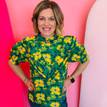 Green floral ruffle top with mock neckline and V-shaped layered ruffle detailing.