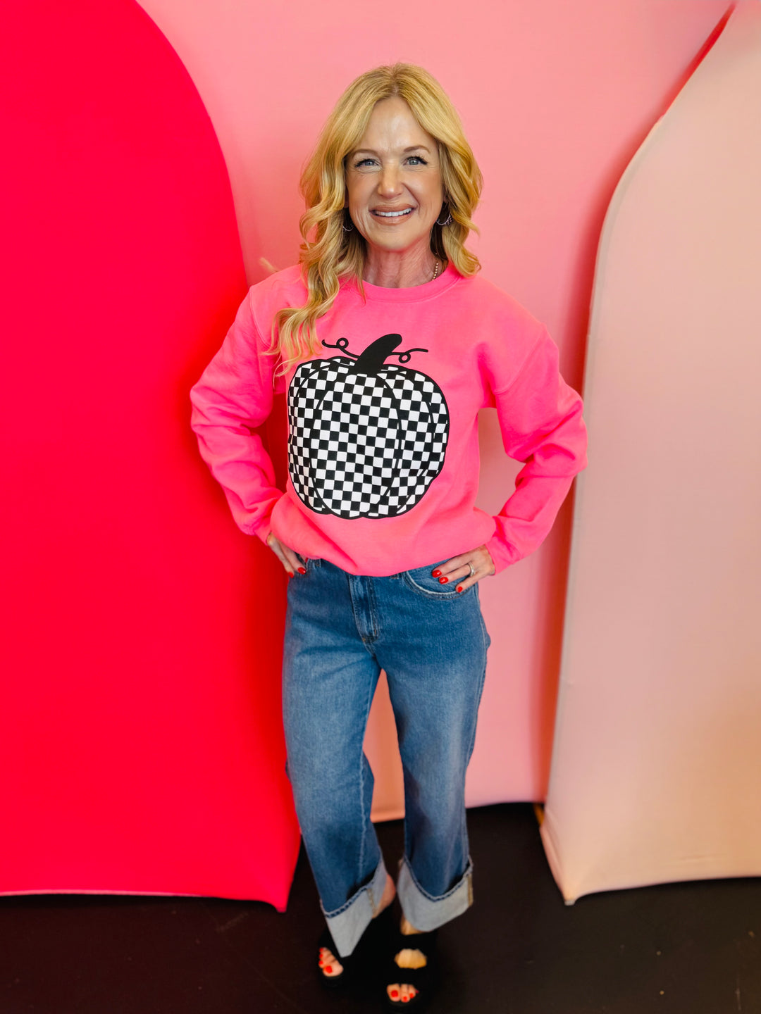 Neon pink crewneck sweatshirt with bold black and white checkered pumpkin graphic, perfect for fall