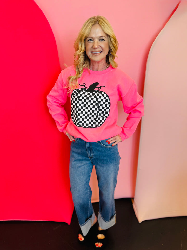 Neon pink crewneck sweatshirt with bold black and white checkered pumpkin graphic, perfect for fall