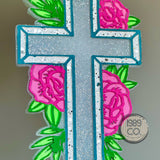 Floral cross car freshie with hook and string hanging from rearview mirror.