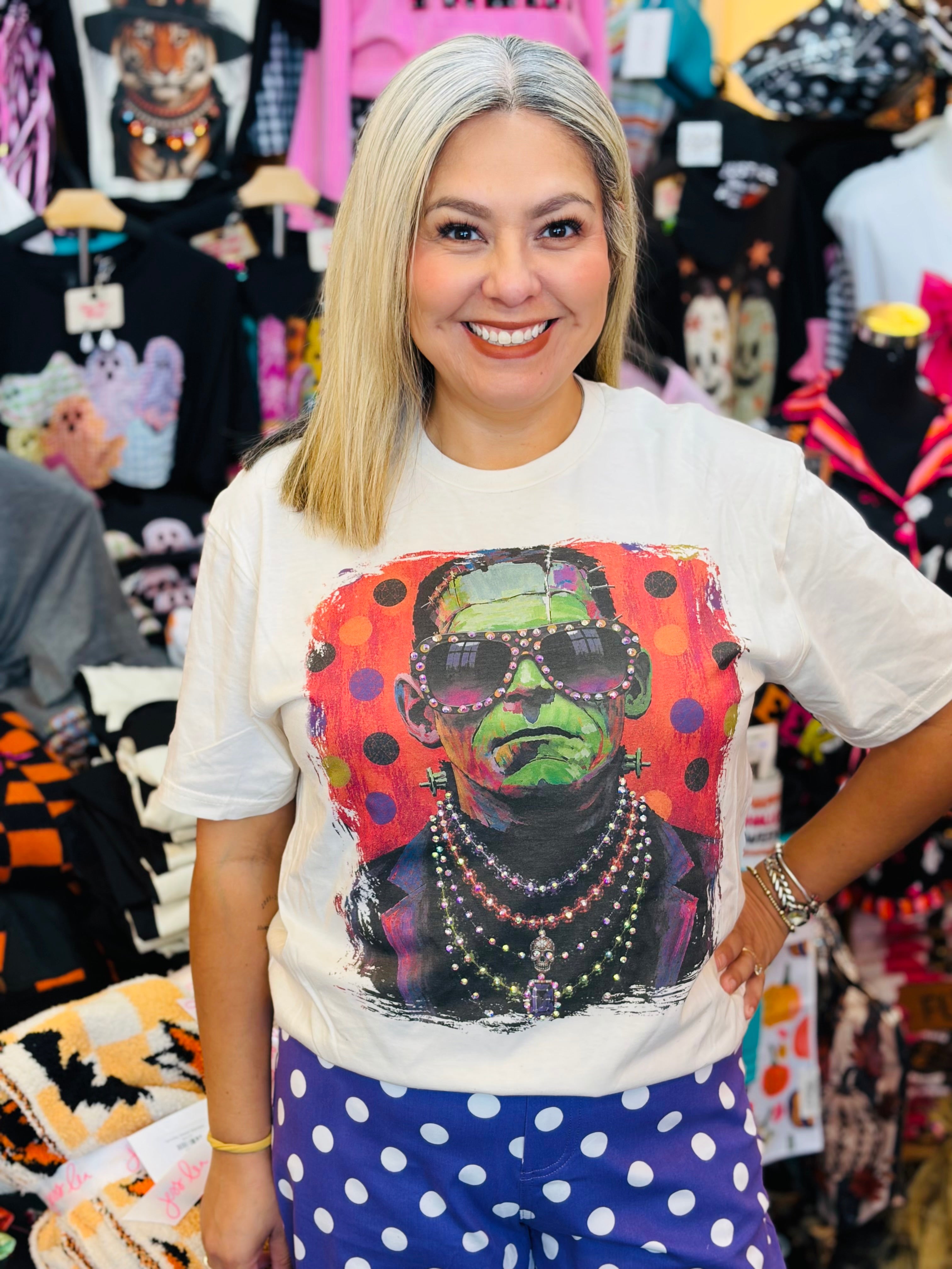 Cream tee with colorful Frankenstein, oversized sunglasses, layered necklaces, rhinestones, and polka dots.