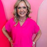 Fuchsia woven blouse with V-neckline and cuffed short sleeves.
