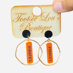 Gold hoops with orange dangle and black writing saying Pirates set on a black stud.