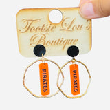Gold hoops with orange dangle and black writing saying Pirates set on a black stud.