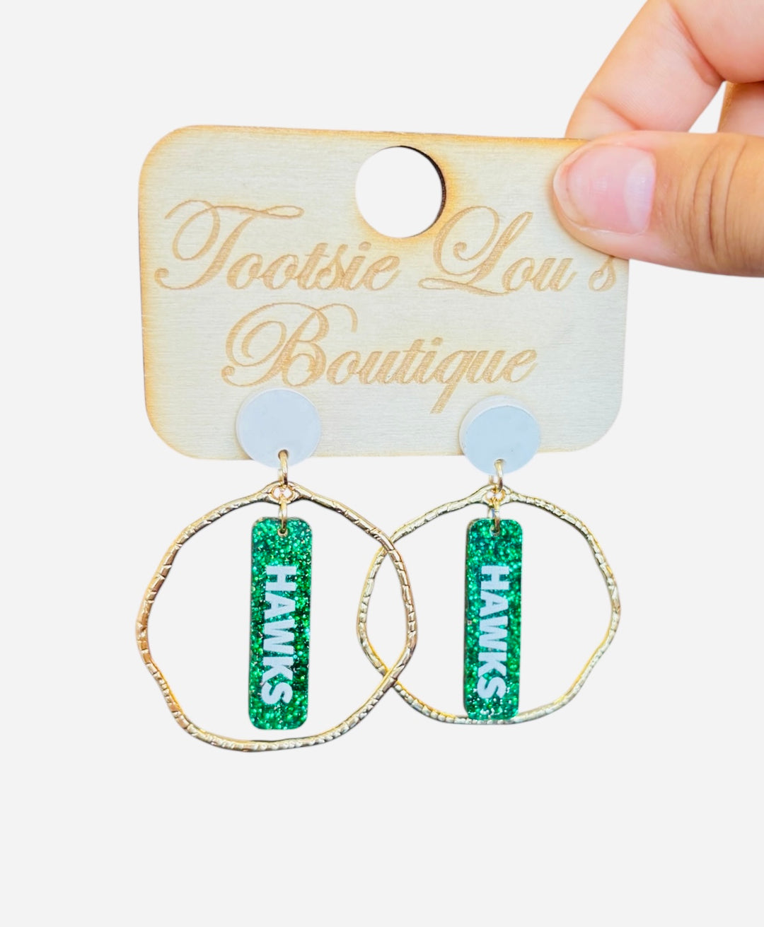 Gold hoops with green glitter dangles and white writing that says Hawks set on a white stud.