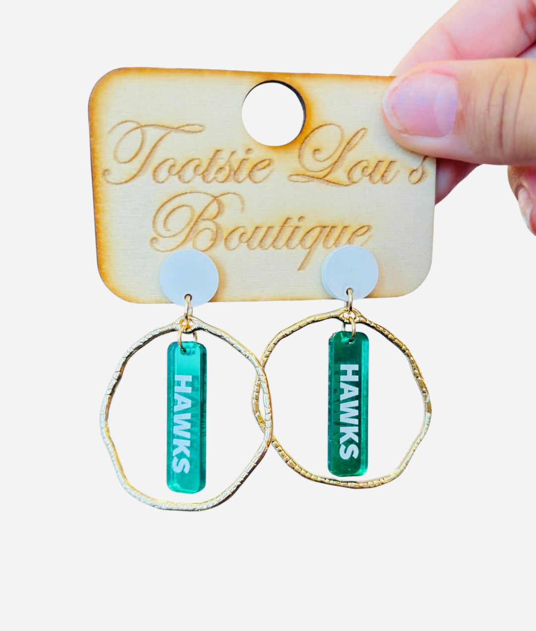 Gold hoops with mirrored green dangles and white writing that’s says Hawks set on white stud