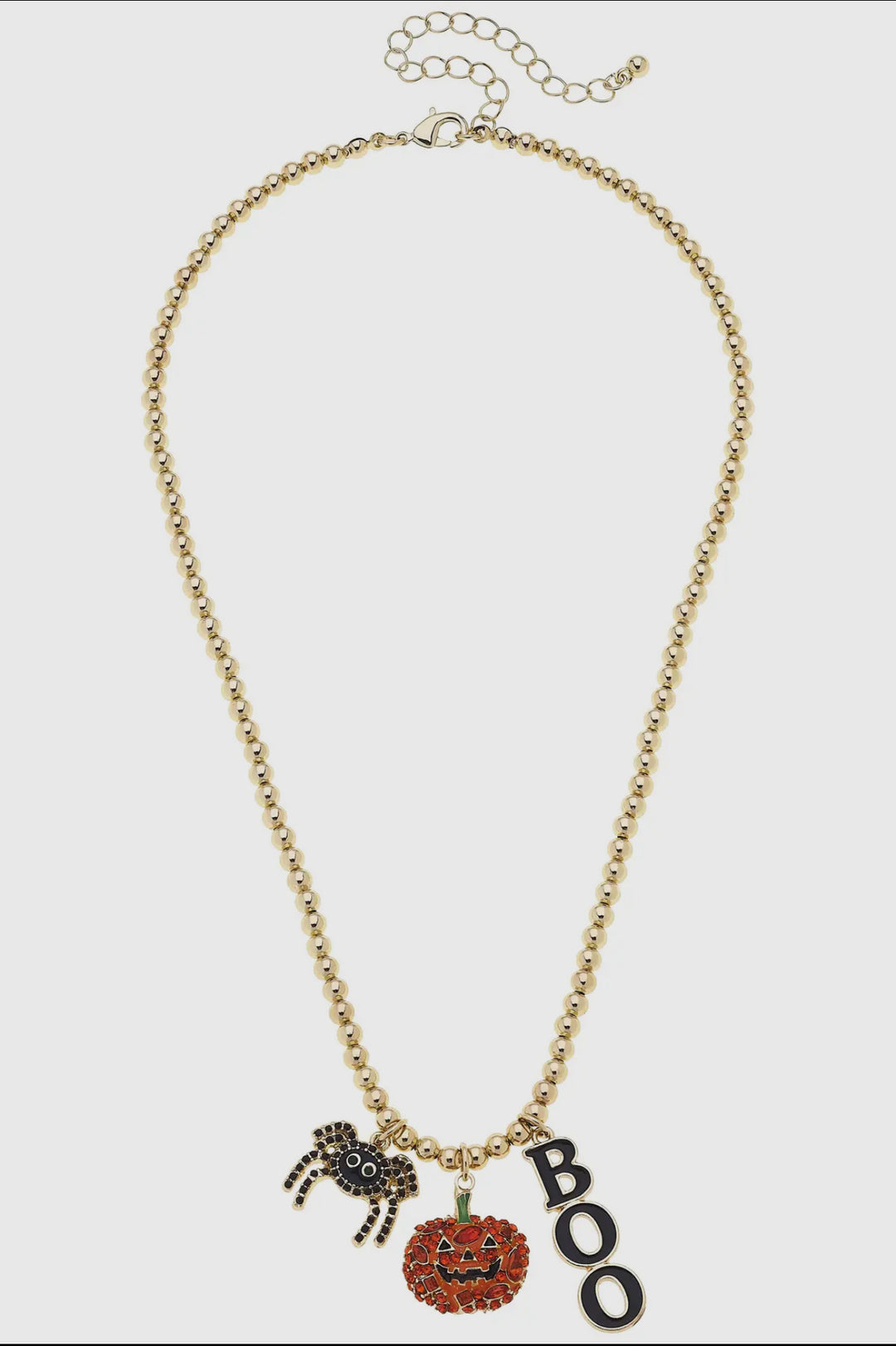 A gold ball bead chain necklace featuring three dangling charms: a glittery orange pumpkin, a black spider, and a charm that spells out the word "BOO."