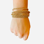 Set of seven gold water-resistant beaded bracelets with stretch fit for effortless stacking and style.
