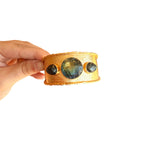 Waterproof gold cuff bracelet with hammered texture and dark oval, teardrop, and round stones.