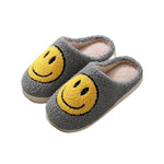 Gray plush slippers with oversized yellow smiley face, soft and cozy for indoor lounging.