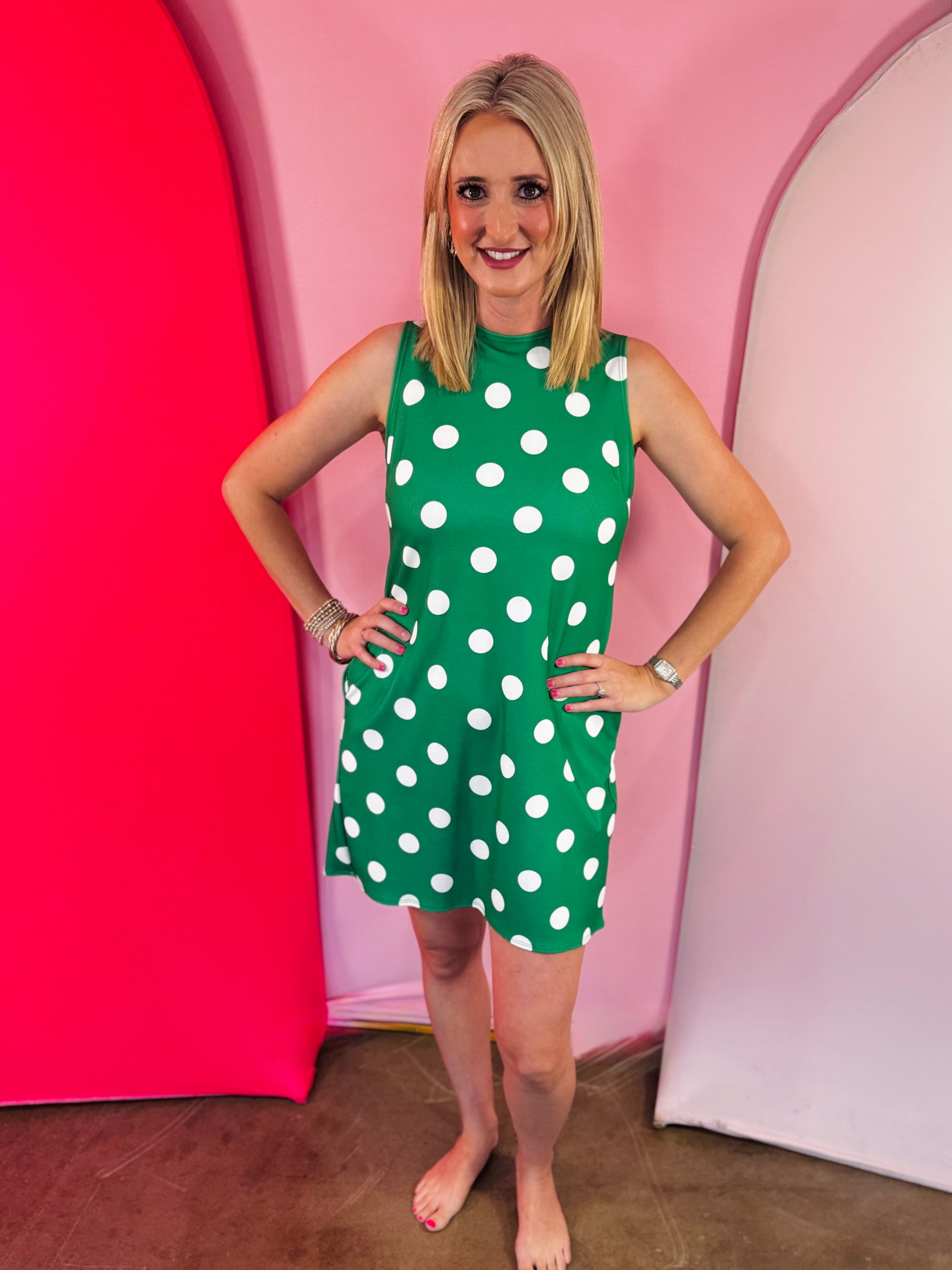 Green sleeveless polka dot dress with oversized bow back detail and side pockets.