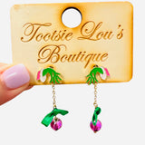 Grinch hand earrings with pink ornament and gold chain, festive holiday dangle jewelry.