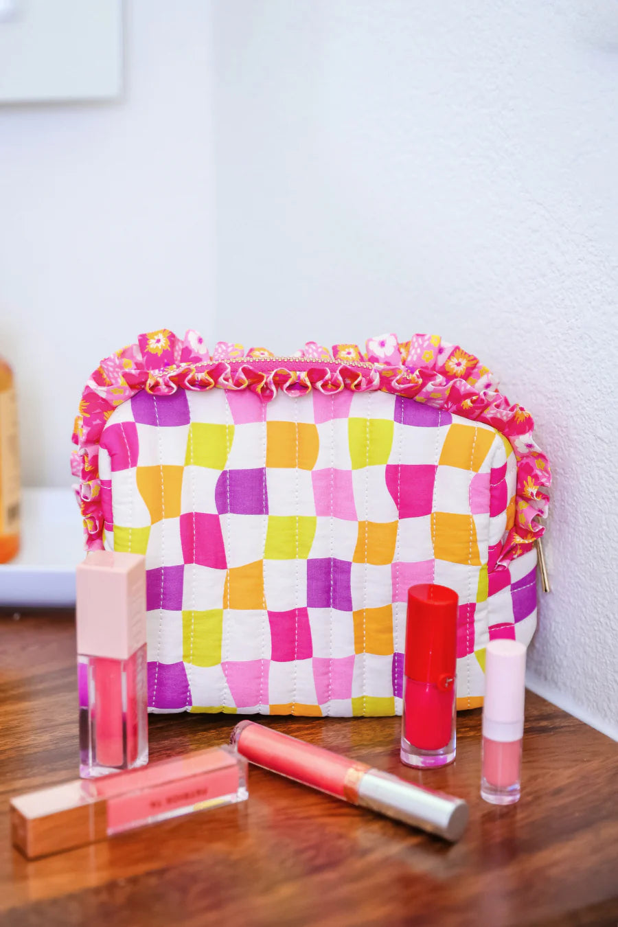 Checkerboard quilted bag with floral ruffle trim and zipper closure.