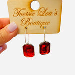 Gold hoop earrings with dangling ruby red emerald-cut stones.