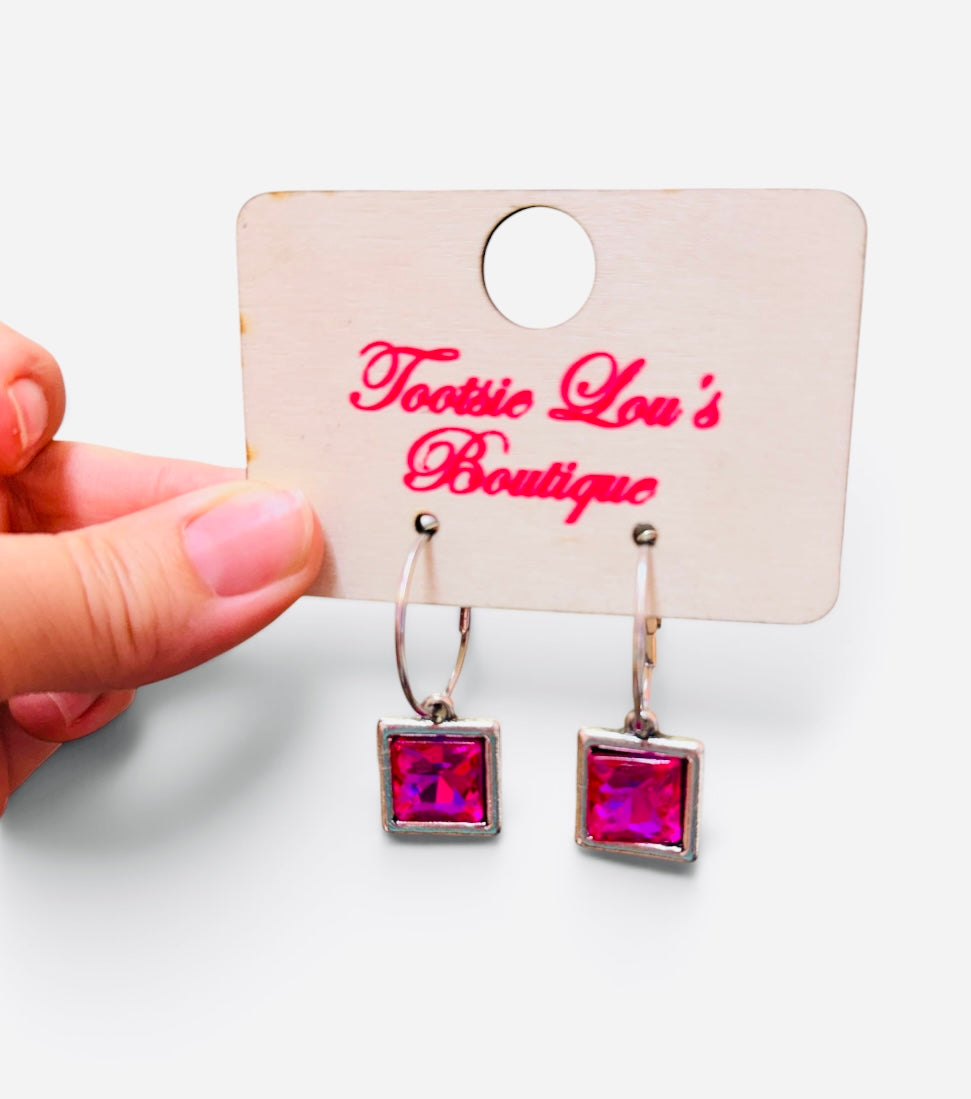 Faceted hot pink square crystal drop earrings suspended from polished silver-tone hoops.