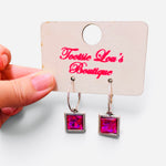 Faceted hot pink square crystal drop earrings suspended from polished silver-tone hoops.